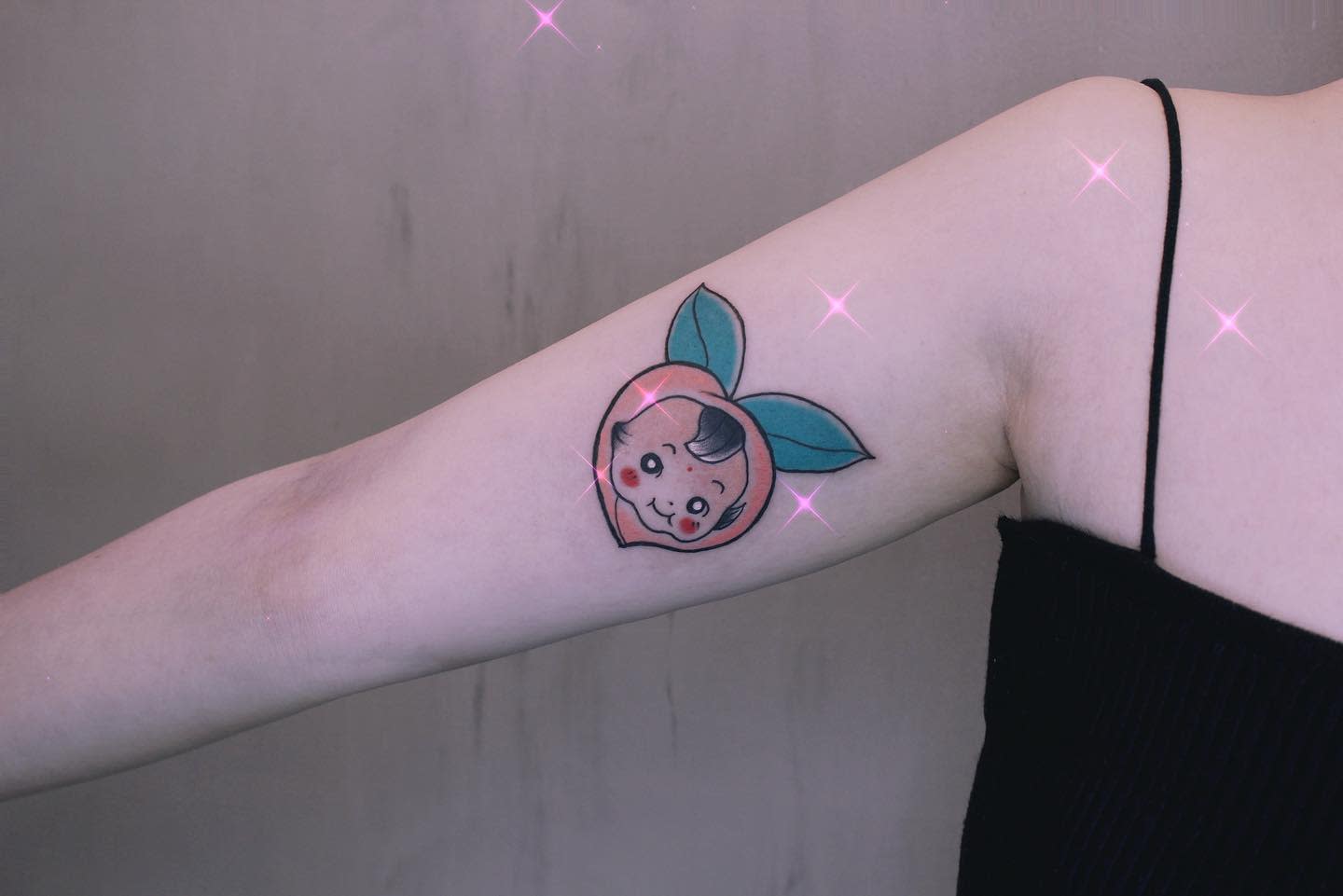 Tattoo of a smiling peach with leaves on an upper arm